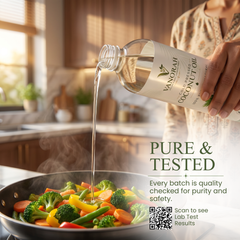 A person in a kitchen pours clear coconut oil from a clear bottle labeled VANORAH COCONUT OIL into a pan of steaming vegetables, with promotional text on the right.